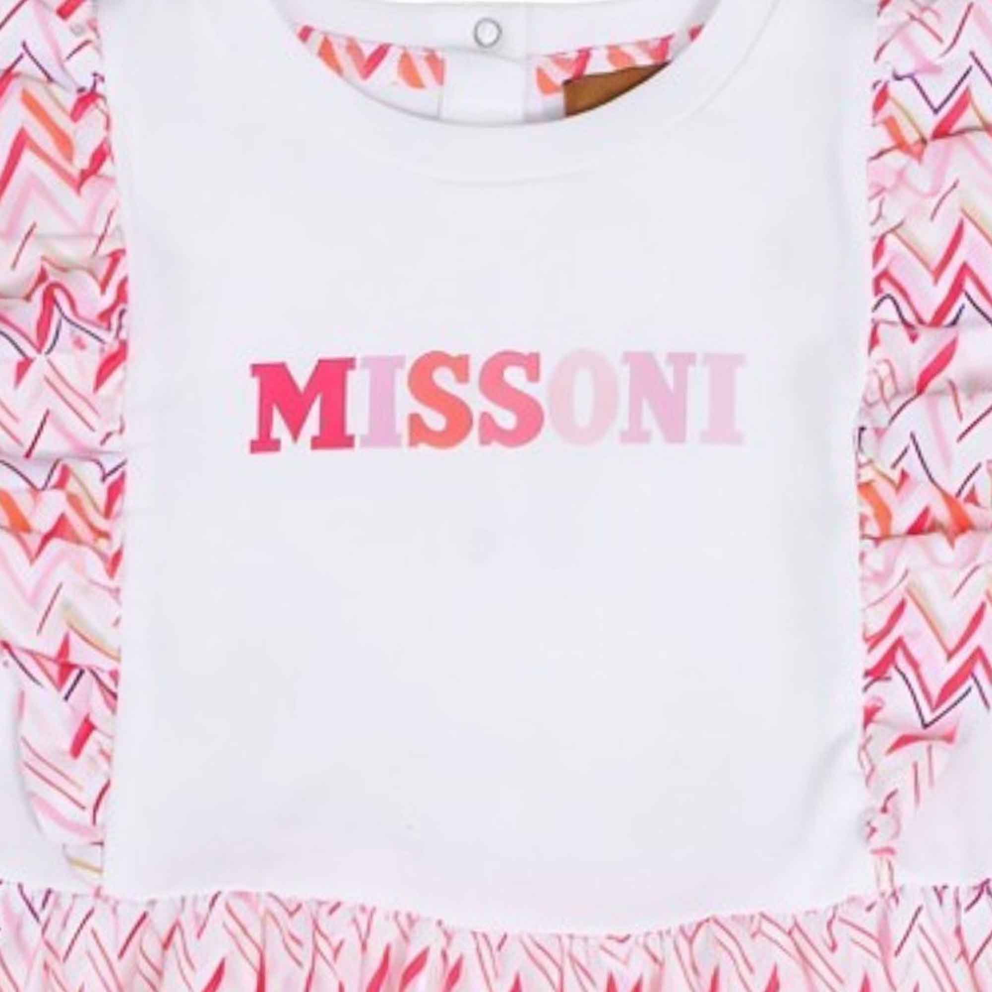 Close-up view of the front bodice of a white Missoni baby dress, showcasing the pink-gradient "MISSONI" logo and signature zigzag ruffles at the shoulders.