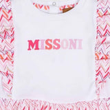 Close-up view of the front bodice of a white Missoni baby dress, showcasing the pink-gradient "MISSONI" logo and signature zigzag ruffles at the shoulders.