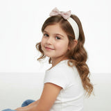 Young girl wearing a white headband with a pink bow on a white background.