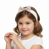 Young girl wearing a white headband with a pink bow on a white background.