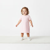 A young toddler girl standing and smiling, wearing a Missoni kids' short-sleeve light pink dress and white sneakers against a white background.