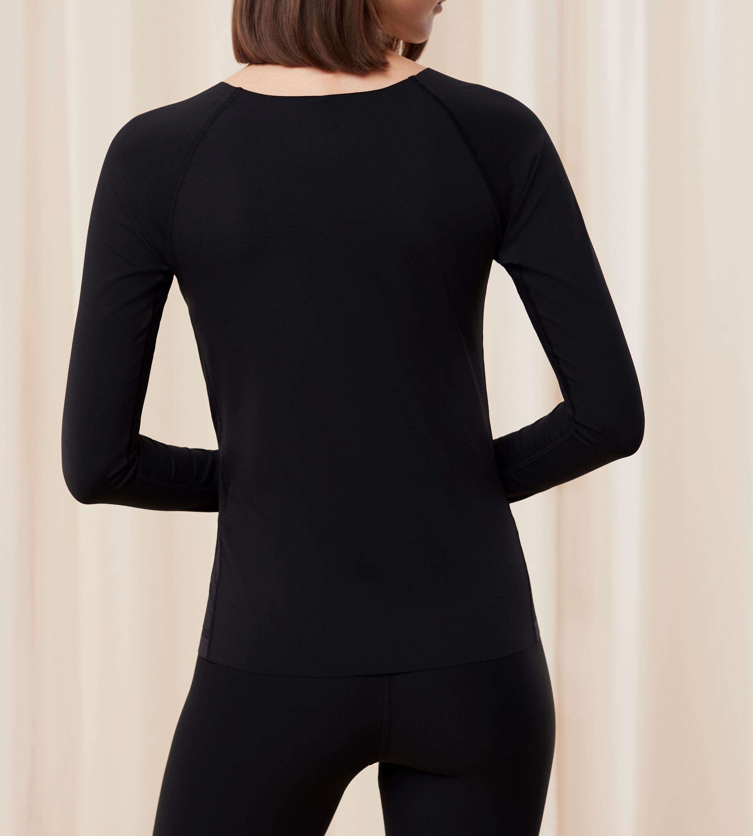Model back view of the Triumph Flex Smart black long-sleeve top, highlighting the smooth fabric and sleek, flexible fit. Available Online Now