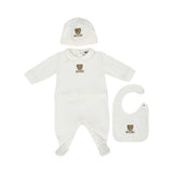 A coordinated three-piece baby gift set in ivory featuring a footed onesie, hat, and bib with Moschino Teddy Bear branding.