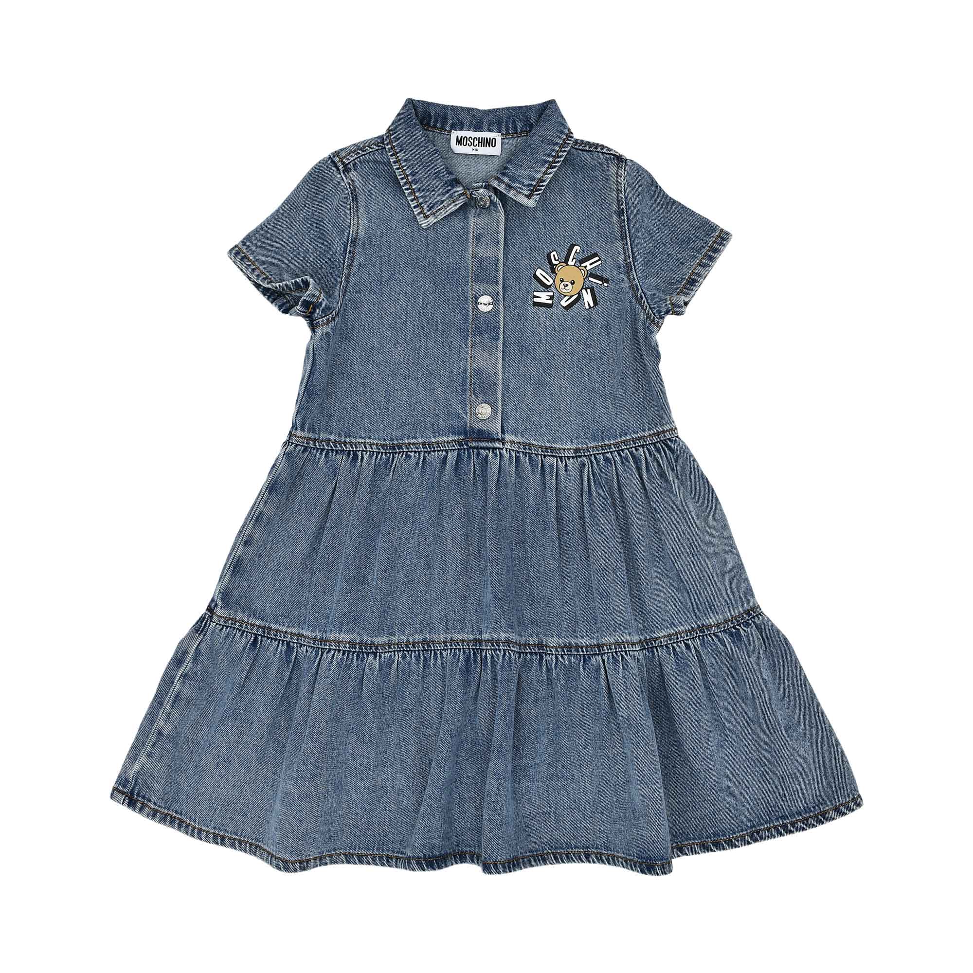 A children's medium-wash blue denim shirtdress with short sleeves, a button-down front, and a tiered ruffled skirt featuring a Teddy Bear logo on the chest.