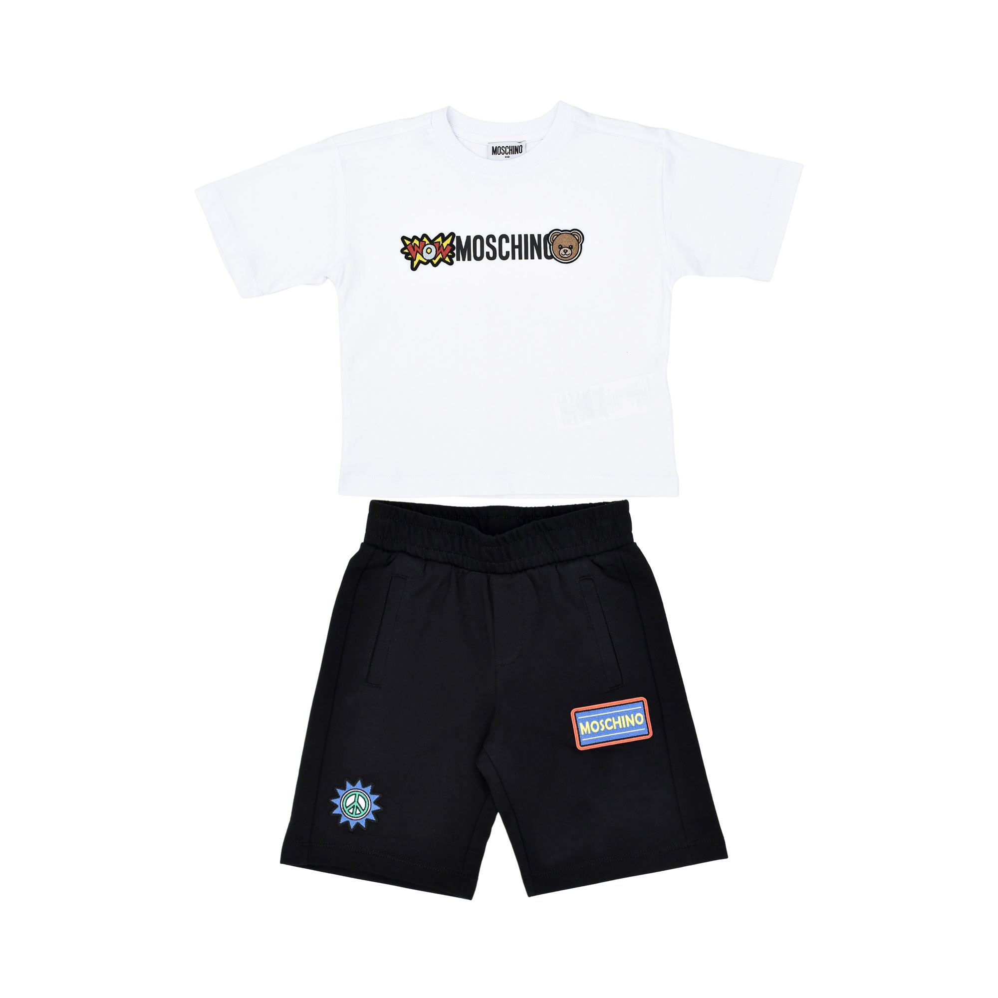 A children's two-piece set featuring a white T-shirt with comic-style Moschino branding and black shorts with graphic patches.