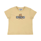 Detailed front view of the beige Moschino Baby T-shirt highlighting the iconic Teddy Bear graphic and brand logo with shoulder popper fasteners.