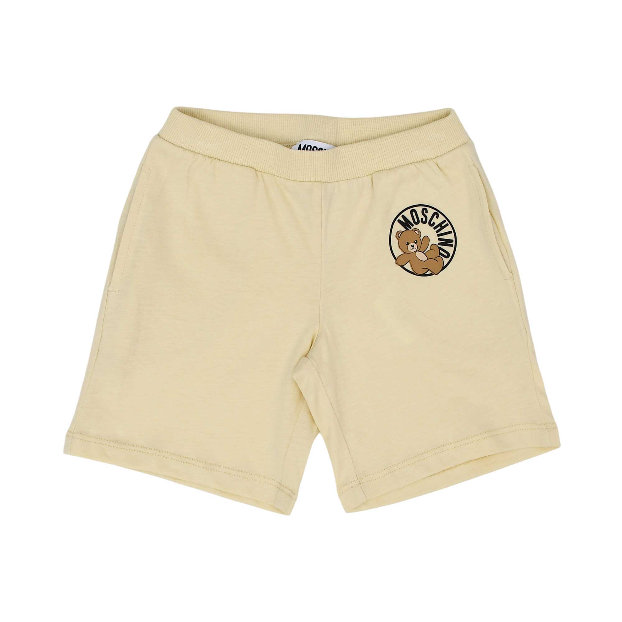 Front view of the buttercream yellow Moschino Baby shorts featuring an elasticated waistband and circular Teddy Bear patch on the left leg.