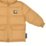 Close-up cropped image focusing on the right side of the Moschino Kids camel jacket, displaying a large front flap pocket, ribbed cuff, zip line, and the vertical brand tag.