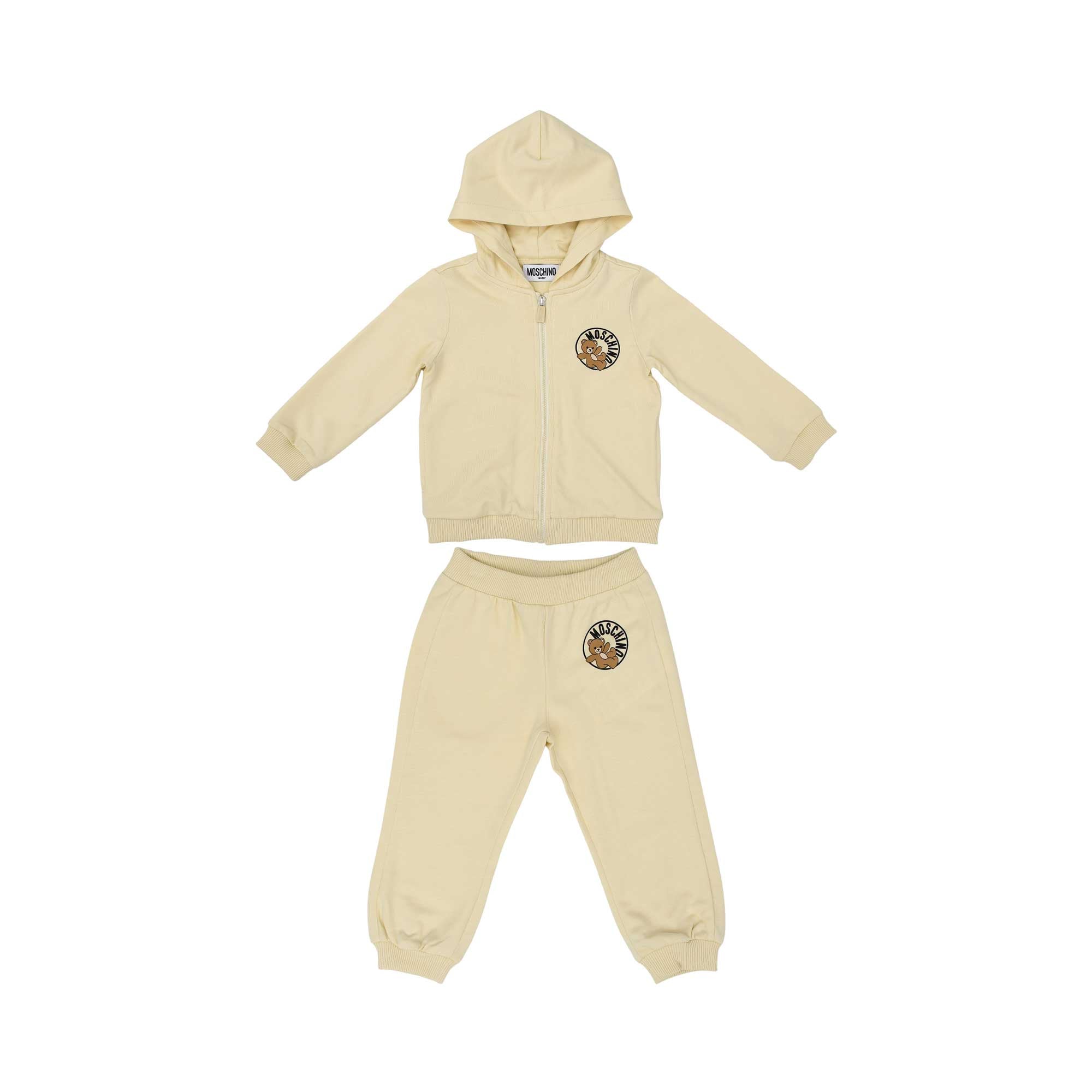 Front view of a cream-colored Moschino Kids tracksuit set consisting of a zip-up hoodie and matching joggers with Teddy Bear patches.