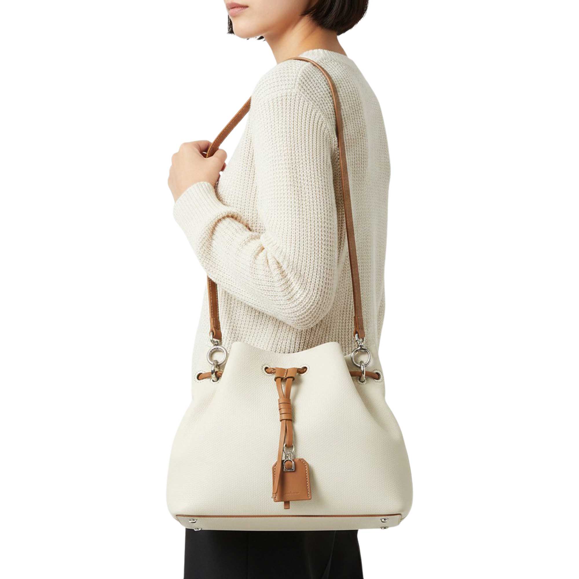 Person wearing a cream sweater with a white handbag featuring brown straps and accents.