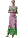 Pink long slip dress with thin straps and green botanical lace trim on the neckline, side slit, and hem.
