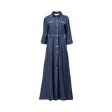 Front studio view of a dark blue denim maxi shirt dress by Nenette against a plain white background, highlighting its button-down front, pointed collar, and metallic chain accents on the chest.