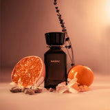 Black NASAJ perfume bottle with oranges and flowers on a soft pink background
