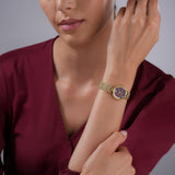 A lifestyle view of the 24mm Escada watch worn on a female wrist, styled with a rich burgundy blouse to accentuate the warmth of the brown wood dial and gold finish.
