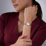 A lifestyle photograph of the 24mm Escada Scarlett gold watch styled on a woman's wrist, pairing with a sophisticated deep burgundy top to highlight the luminous tone of the white diamond dial and metallic textured band.