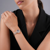 A lifestyle photograph of the 24mm Escada Scarlett rose gold watch styled on a woman's wrist, pairing with a sophisticated black sleeveless vest top to highlight the smoky tone of the grey diamond dial and metallic textured band.