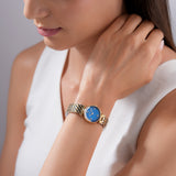 A lifestyle photograph of the Escada Scarlett watch being worn on a woman's wrist, pairing flawlessly with a sleeveless white top to highlight the deep blue dial and elegant mixed-metal scale band.