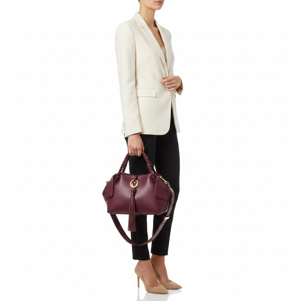 Model in a white blazer and black trousers holding the luxury burgundy leather handbag by its braided handles, showcasing its real-world proportions and styling, available at BLUE SALON.