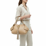 Woman holding a beige handbag with tassel on a white background.