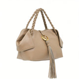 Left three-quarter studio view of a premium beige leather handbag featuring unique folded side wings, braided top handles, and a signature gold-tone logo emblem with a long leather tassel, available at BLUE SALON.