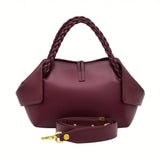 Rear studio view of the burgundy leather handbag showing the clean leather back panel, stitched center tab, braided handles, and unattached matching leather shoulder strap laid in front, available at BLUE SALON.