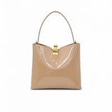 Front view of the beige patent leather bag styled with its wide, detachable matching shoulder strap attached.