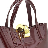 Extreme close-up of the bag's secure gold-tone metallic hardware clasp, showcasing an engraved circular emblem design between the dual top handles.