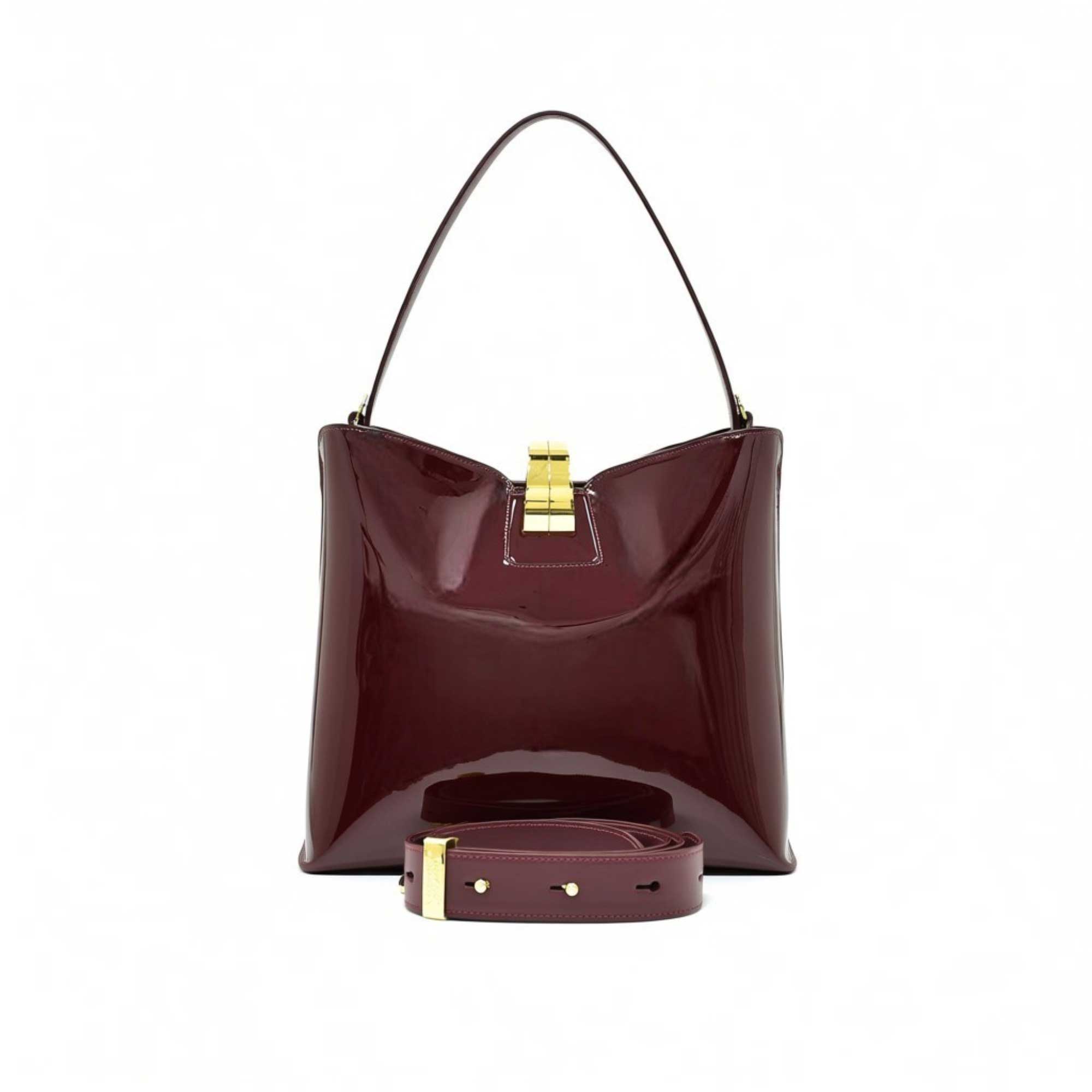 Front view of the burgundy patent leather bag styled with its wide, detachable matching shoulder strap attached.