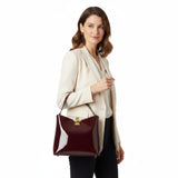 Woman holding a burgundy handbag against a white background.
