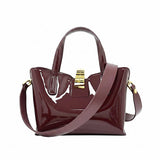 Rear view of the burgundy patent leather handbag, displayed with its detachable matching leather shoulder strap neatly rolled and resting in front.
