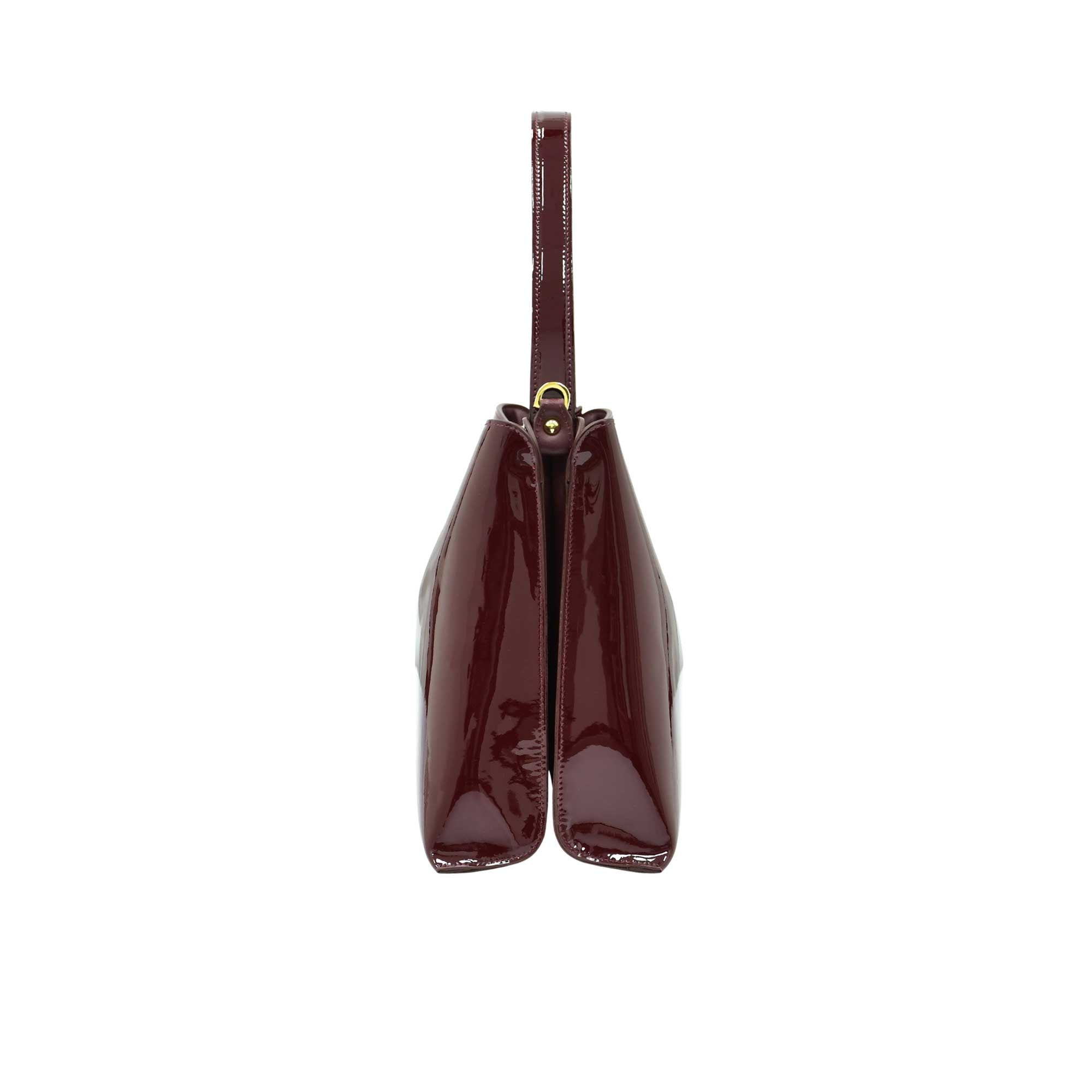 Side profile view of the sleek burgundy patent leather handbag showing its structured dual-compartment gusset design.