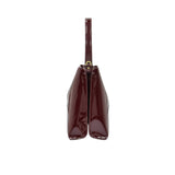 Side profile view of the sleek burgundy patent leather handbag showing its structured dual-compartment gusset design.