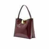Three-quarter perspective view of the glossy burgundy patent leather handbag, showcasing its gold-accented hardware.