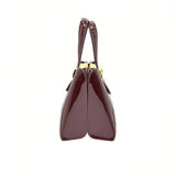 Side profile view of the glossy burgundy handbag, highlighting its distinct dual-compartment accordion gusset construction.