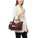Woman holding a burgundy handbag against a white background.