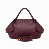 Rear view of the burgundy leather handbag with the detachable shoulder strap neatly rolled in front against a white background.