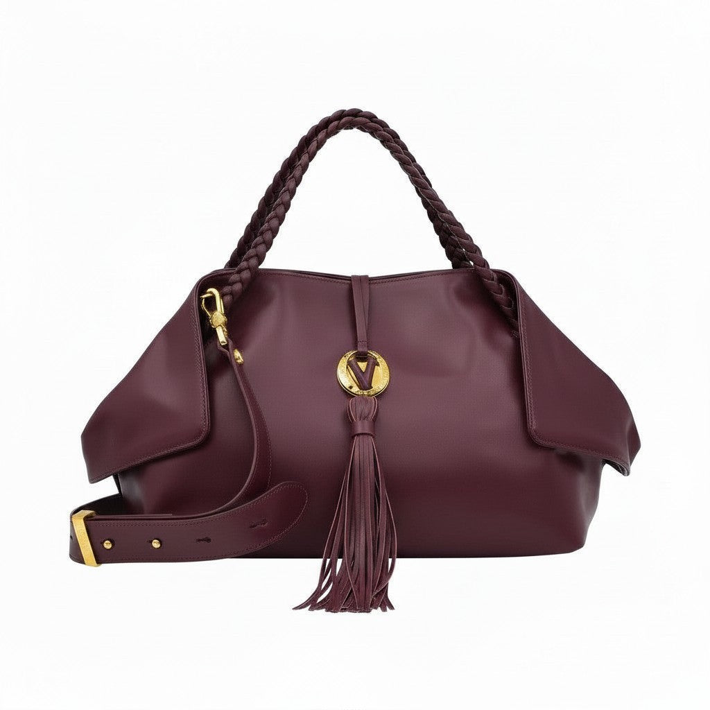 Front view of a burgundy leather handbag with braided handles, a large leather tassel, and a matching detachable shoulder strap.