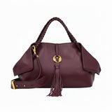 Front view of a burgundy leather handbag with braided handles, a large leather tassel, and a matching detachable shoulder strap.