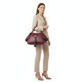 Woman holding a maroon handbag against a white background.