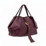 Three-quarter right angle view of the burgundy leather handbag, highlighting its unique folded side panels and long leather tassel.