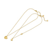 A side-by-side close-up studio presentation of the Escada Giselle set, showing the larger gold-plated heart pendant with an engraved EE monogram and the smaller gold heart pendant with a single corner crystal and a chain logo link.