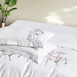 A pair of luxury white pillowcases featuring vertical floral embroidery and clean flanged edges.
