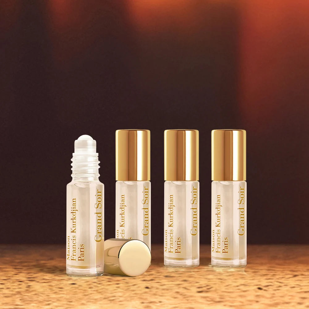 Four clear glass roll-on perfume bottles. Three have gold-toned caps; one is uncapped, showing a white applicator, its cap ly