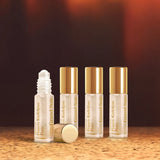 Four clear glass roll-on perfume bottles. Three have gold-toned caps; one is uncapped, showing a white applicator, its cap ly