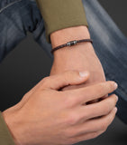 Brown braided leather bracelet with a central black cylinder flanked by two silver-toned rings.