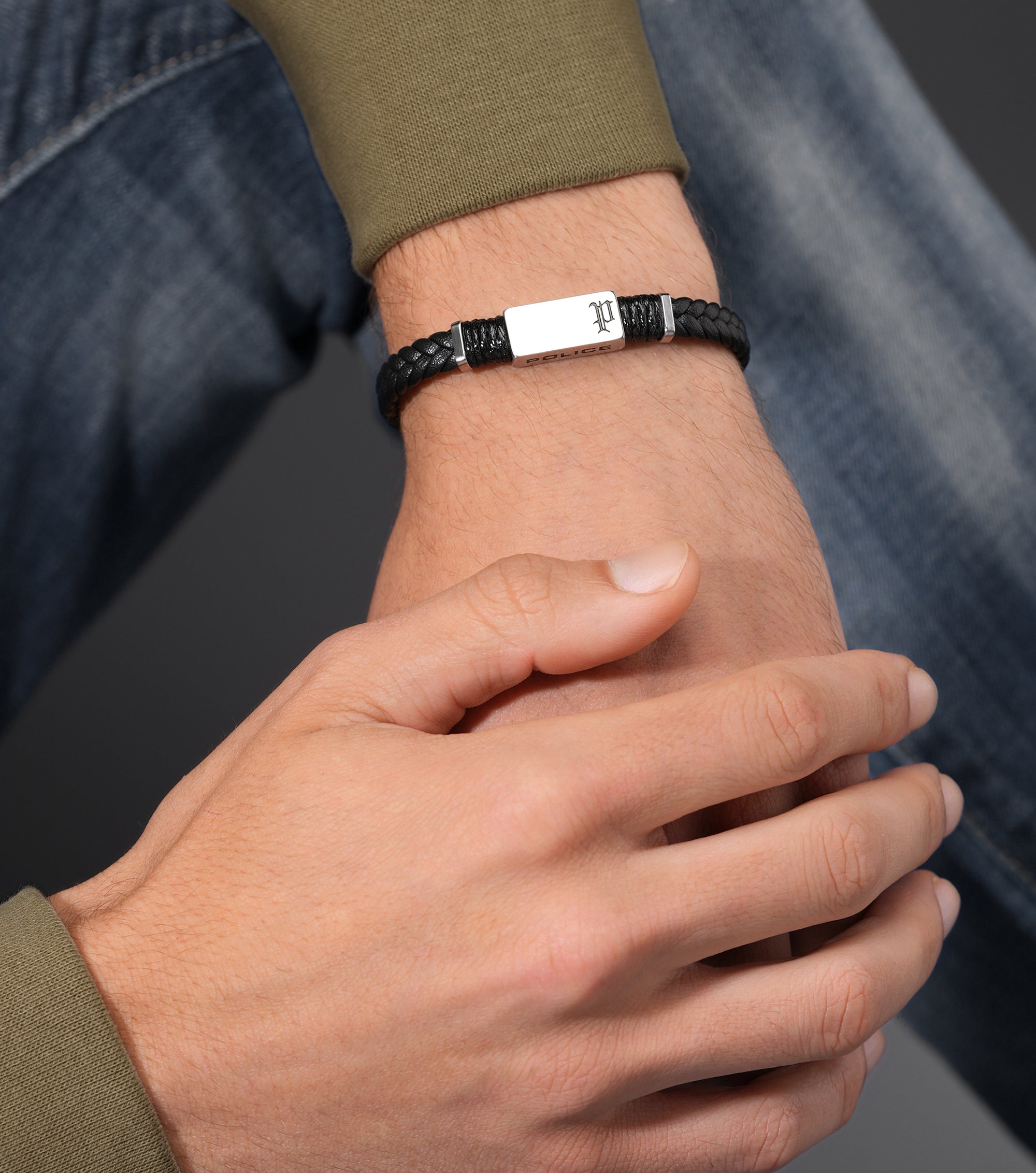 Black braided leather bracelet with a silver-toned rectangular bar engraved with a stylized 'P' and 'POLICE', flanked by silv