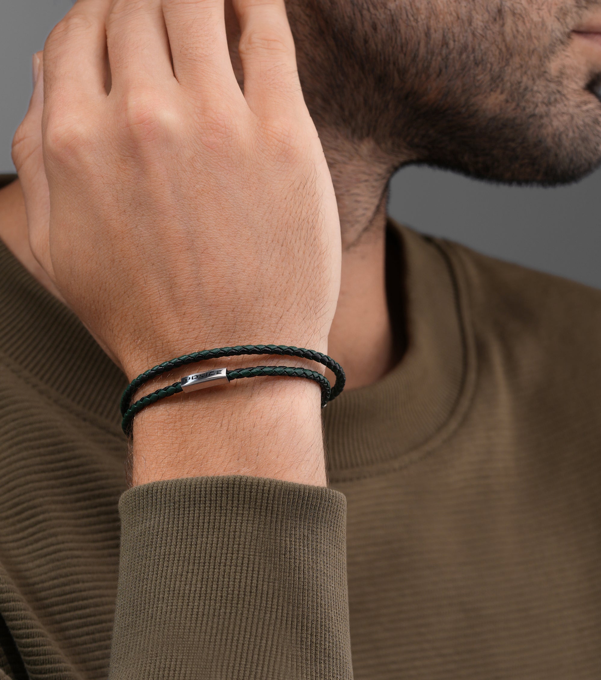 Black-green double-wrap braided leather bracelet with a silver-toned rectangular bar engraved 'POLICE'.