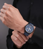 Round black-toned watch with a blue textured dial, two sub-dials, silver-toned hands, and a blue leather strap.
