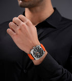 Silver-toned angular watch with a gunmetal textured dial, white numbers, blue accents, and a bright orange silicone strap.