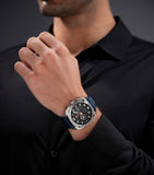 Silver-toned cushion-shaped watch with a dark gray textured dial, white numerals, orange accents, and a blue leather strap.